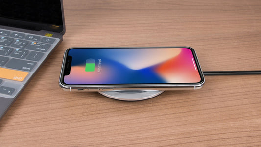 Smartphone iPhone 16 on a wireless charging pad with a laptop in the background on a wooden surface
