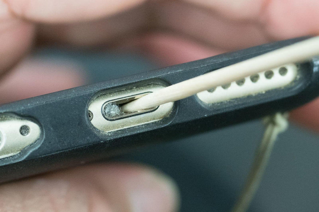 Close-up of a phone case with a cable and dirty charging port, held by a person.