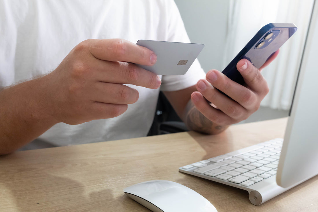 Person holding a smartphone and credit card with a laptop on a desk