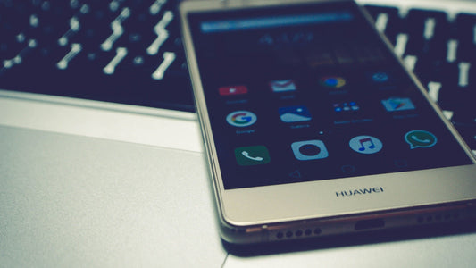 A silver Huawei smartphone with its screen on, resting on a metallic surface in front of a blurred keyboard.