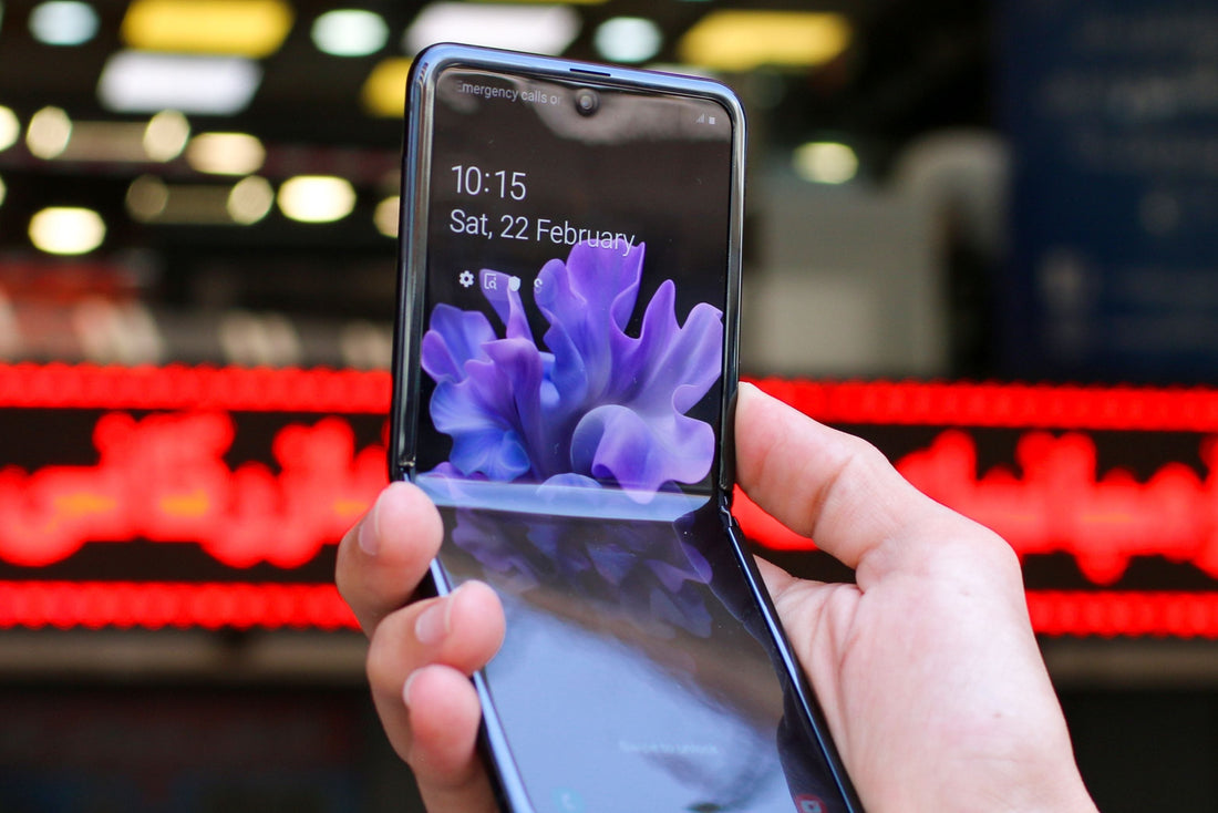 Person holding a foldable Samsung Galaxy Z Flip smartphone with a colourful display in front of a blurred indoor background