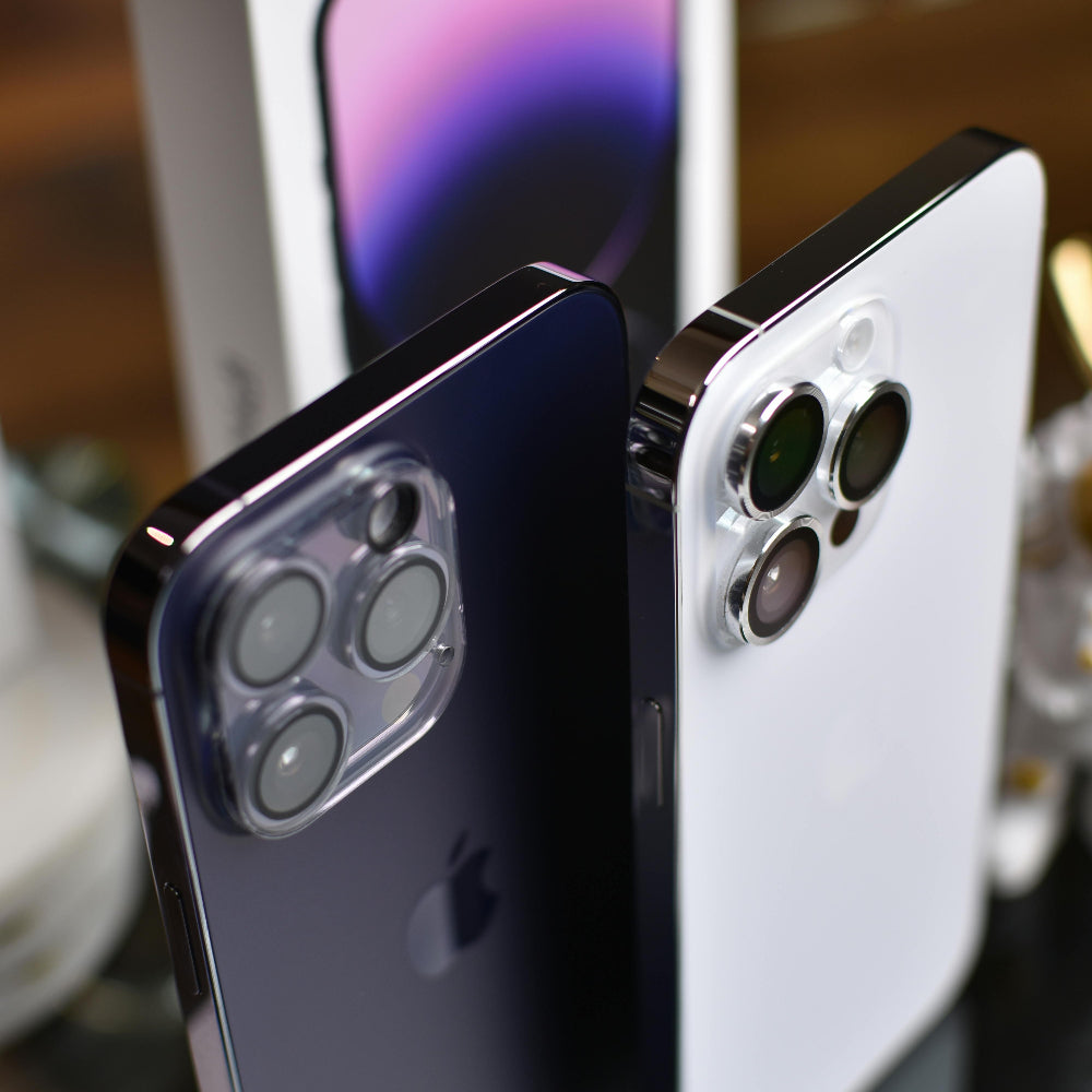 Two iPhone 14 Pro Max, one black and one white, displayed with a blurred phone box in the background.