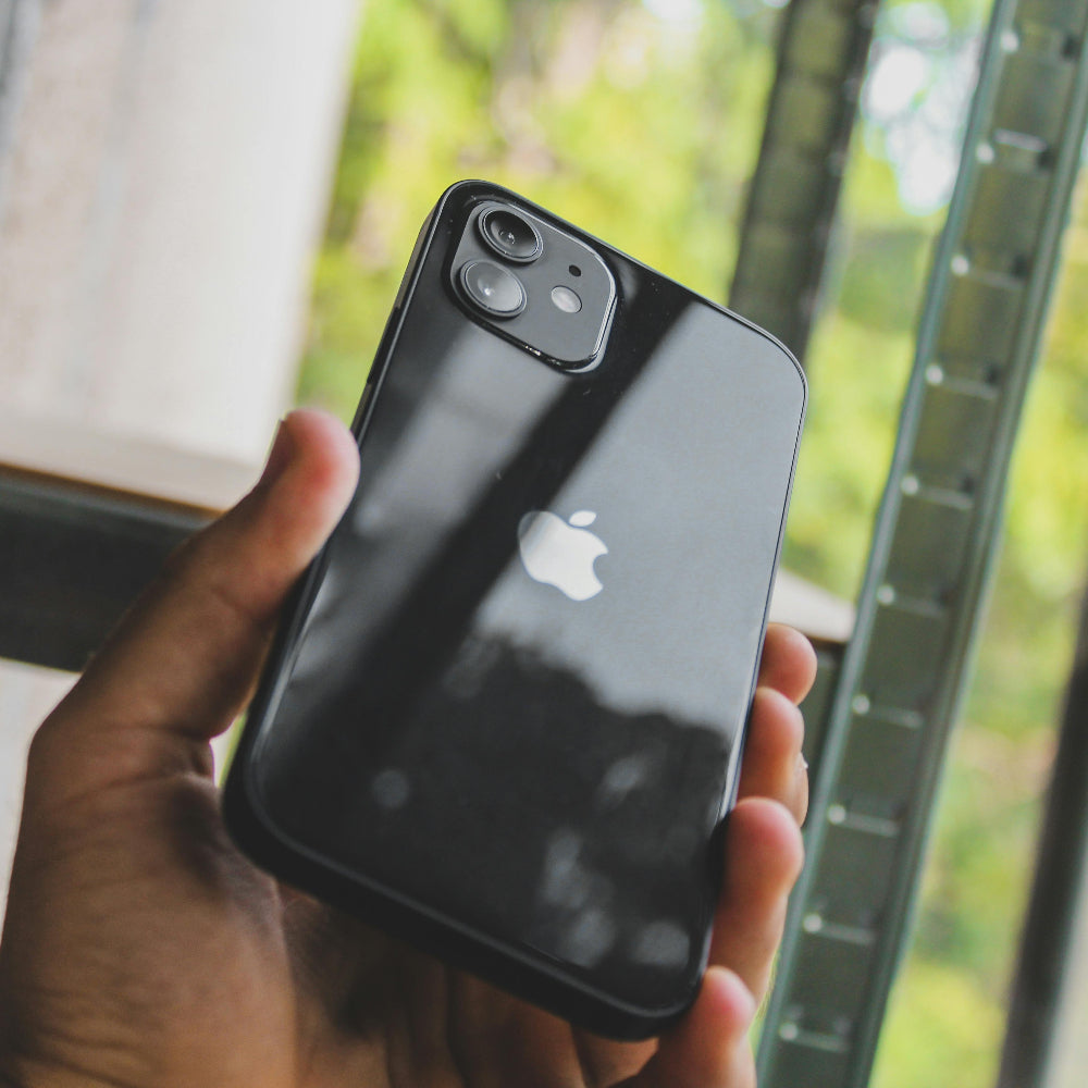 Person holding a black iPhone with an Apple logo, blurred greenery in the background